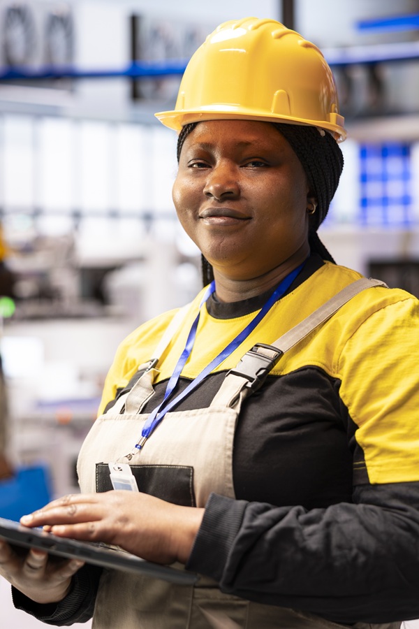 Portrait of female automation expert overseeing optimization of robot arm and assembly line in industrial plant. Closeup of african american industry 4.0 engineer in smart factory, looking at camera.